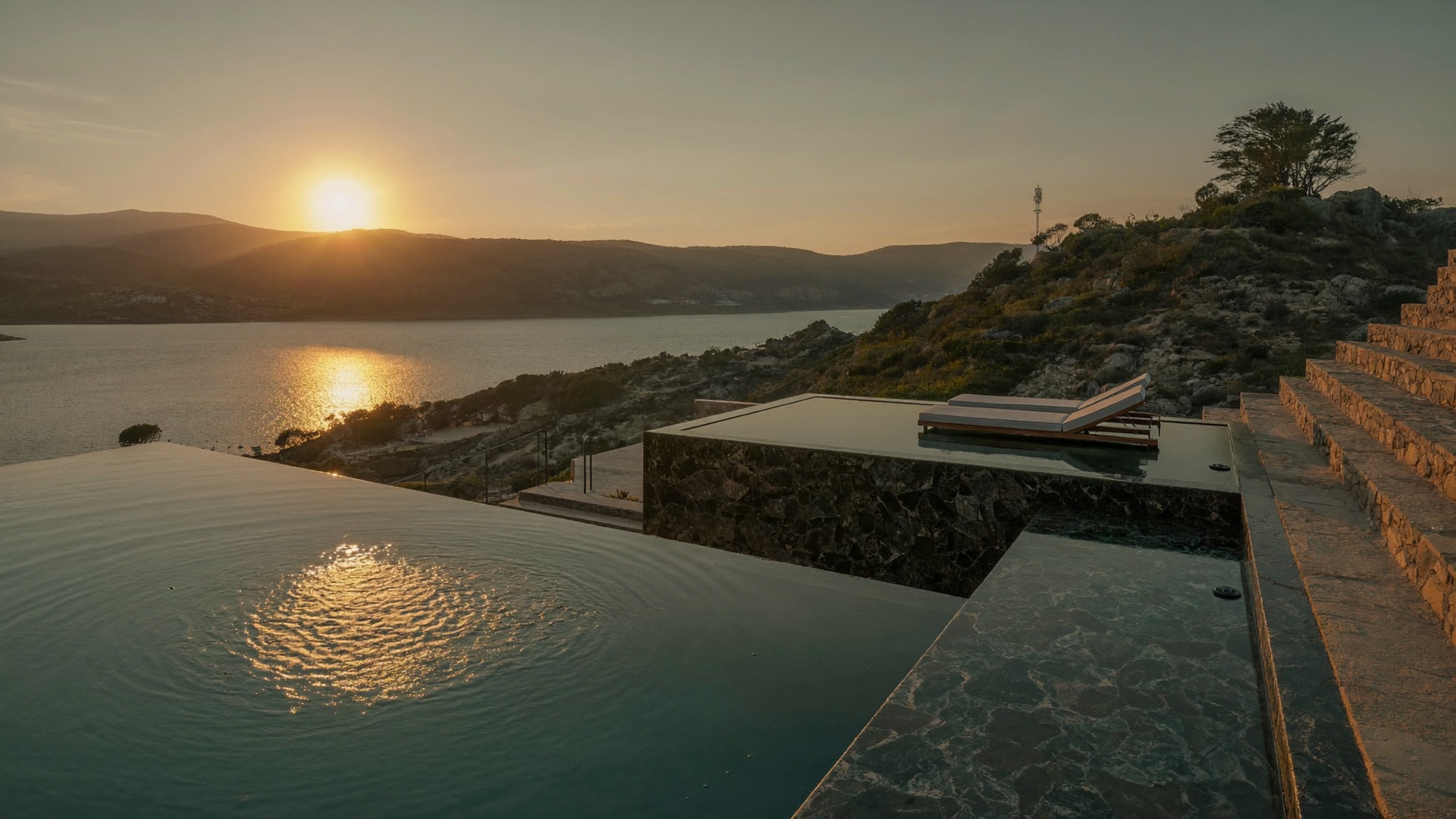 Terraced hillside pool and spa above Lake Travis at sunset with stone-clad walls